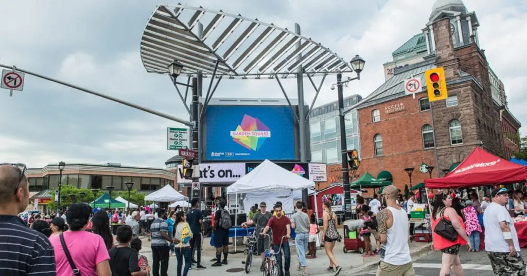 Crowd at Brampton downtown festival with tents, stage, and historic building in background.