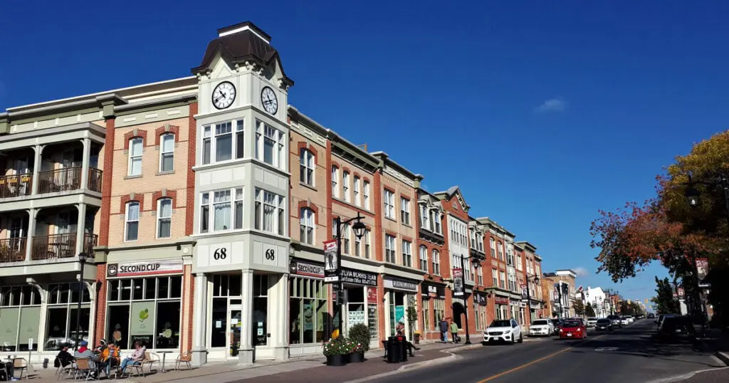 Corner building with clock tower in Markham, Ontario, featuring shops and cafes on a sunny day.