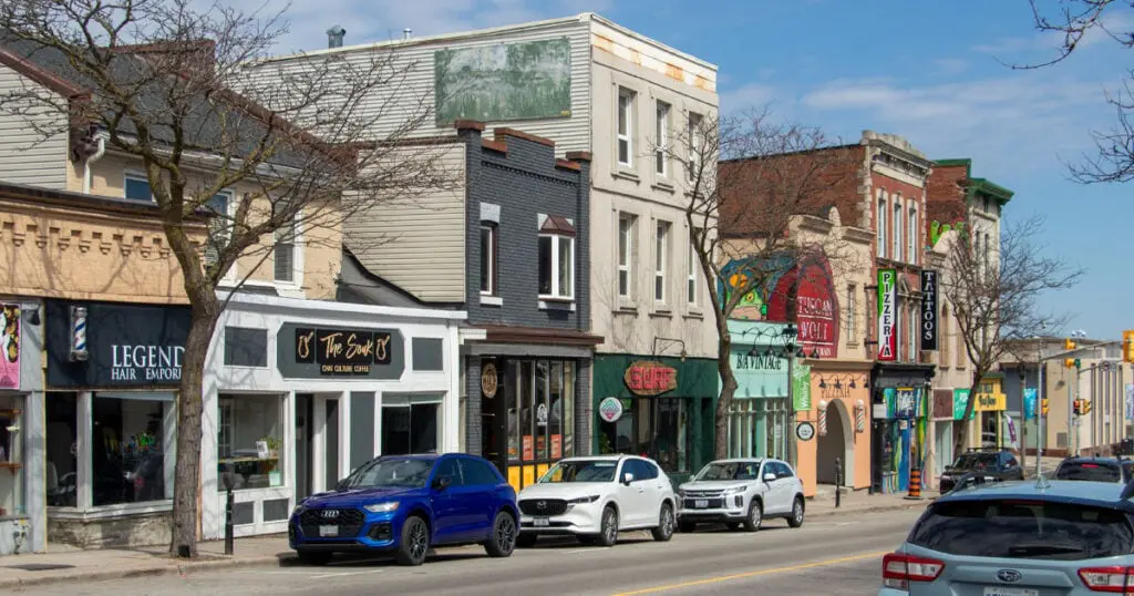 Vibrant street scene in Whitby, Ontario with shops, cafes, and parked cars on a sunny day.