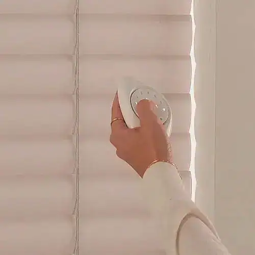 Close-up of hand using a cleaning device on white window blinds.