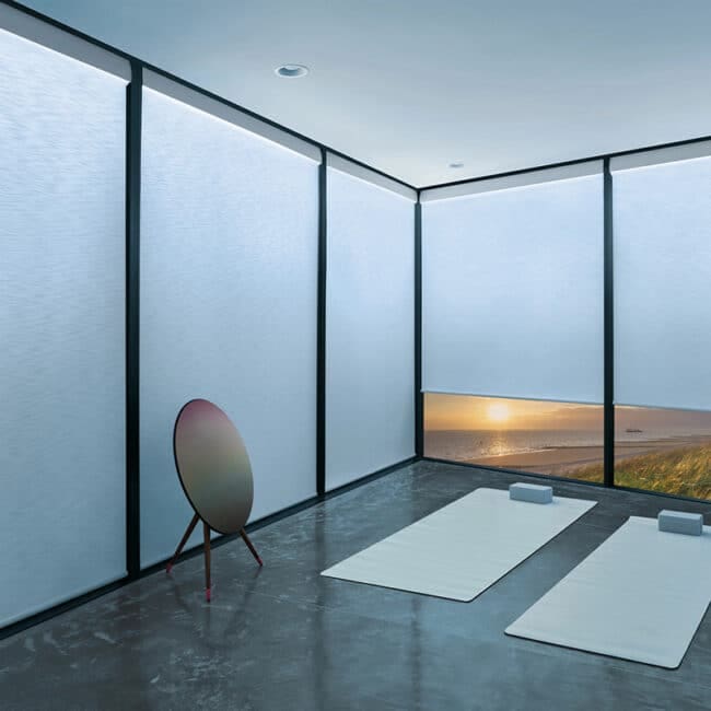 Bright modern yoga space with large windows and ocean sunset view, minimal decor, mats, blocks, and meditation accessories for relaxation and mindfulness.