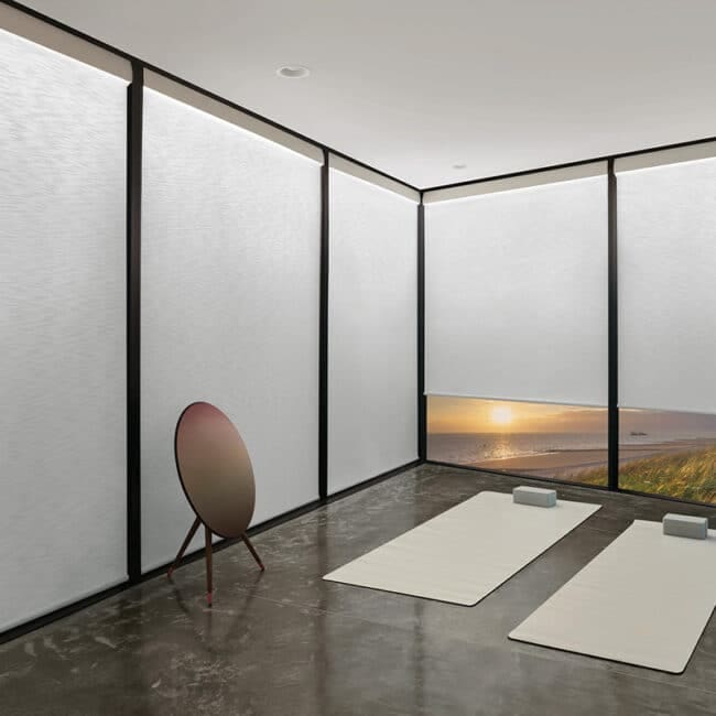 Bright modern yoga studio with large windows overlooking scenic beach sunset, minimalist decor, yoga mats, bolster cushions, and tranquil ambiance for relaxation and mindfulness.