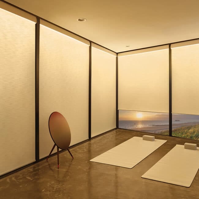 Bright, peaceful yoga studio with large windows overlooking the beach during sunset, minimal decor, yoga mats, and calming atmosphere for relaxation and meditation.