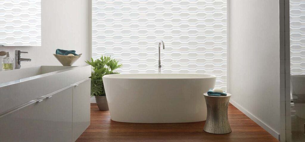 Luxurious white bathtub in contemporary bathroom featuring textured wall, wooden floor, and elegant decor.