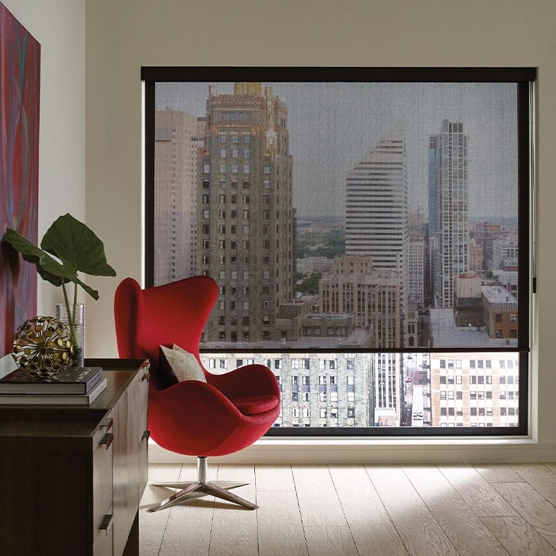 Modern city skyline visible through large window with roller shade in high-rise apartment.