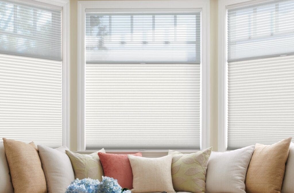 Bright living room with white window blinds, beige sofa, and assorted throw pillows with floral and textured designs.