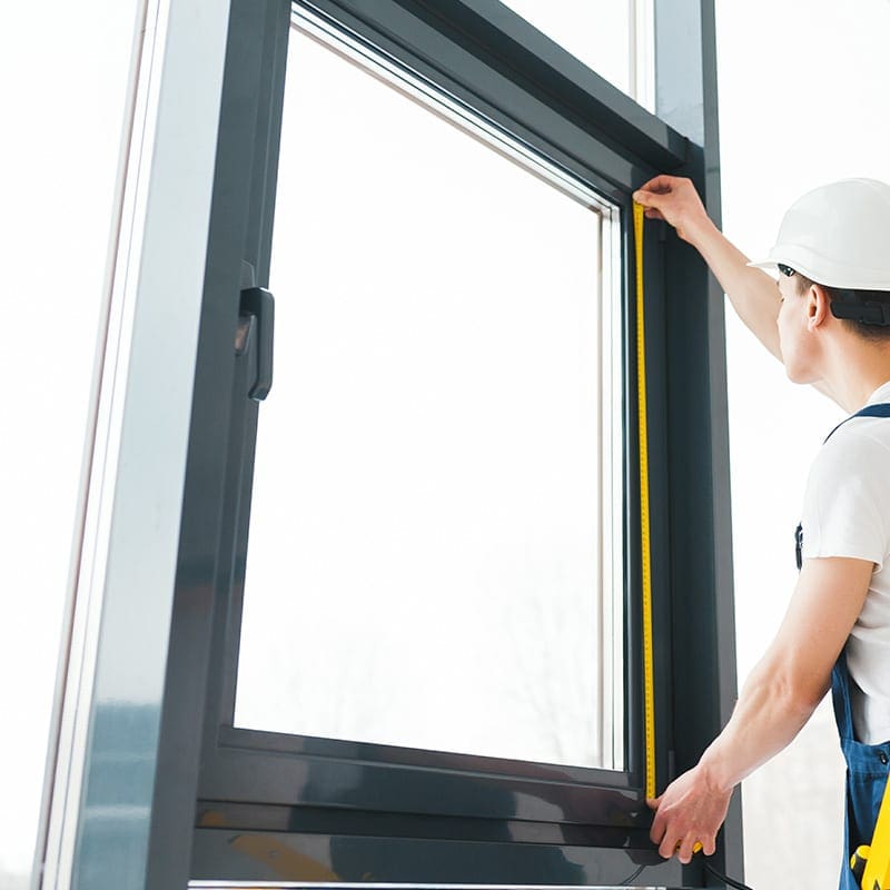 Skilled worker measuring house window frame with tape measure for proper installation and fitting, ensuring quality craftsmanship.