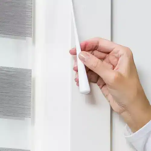 Close-up of a hand cleaning window blinds with a white brush, demonstrating dust removal and maintenance for clean, bright window treatments.