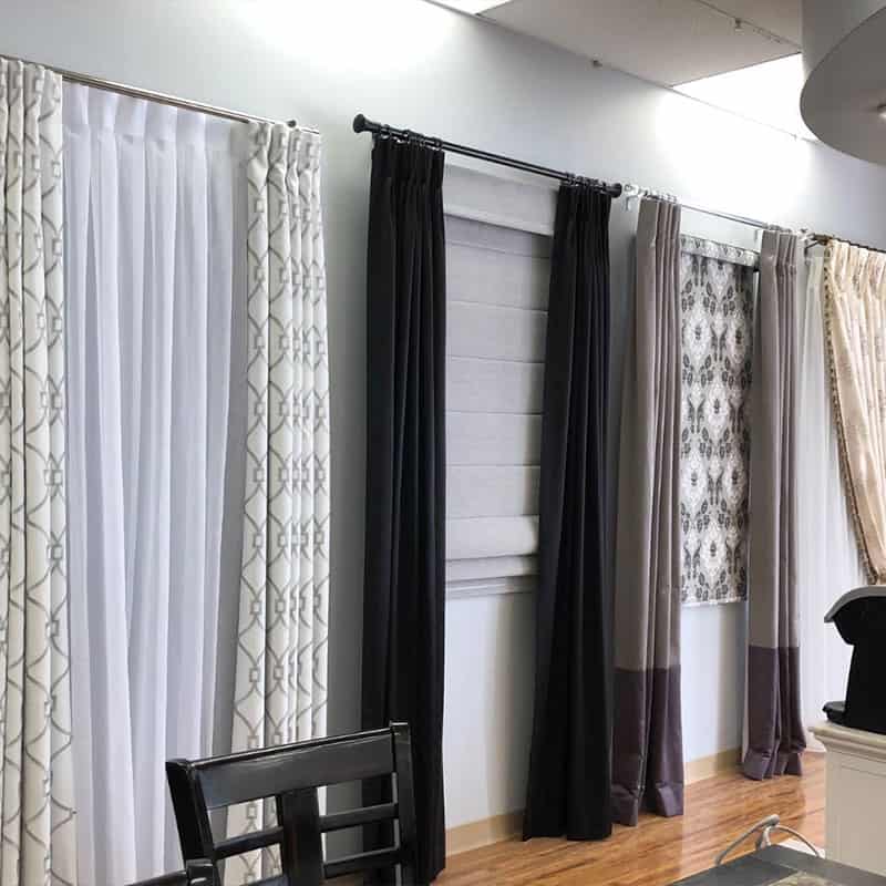 Collection of stylish curtains in various colors and patterns displayed in a home decor showroom, showcasing different fabric textures and designs for window treatments.