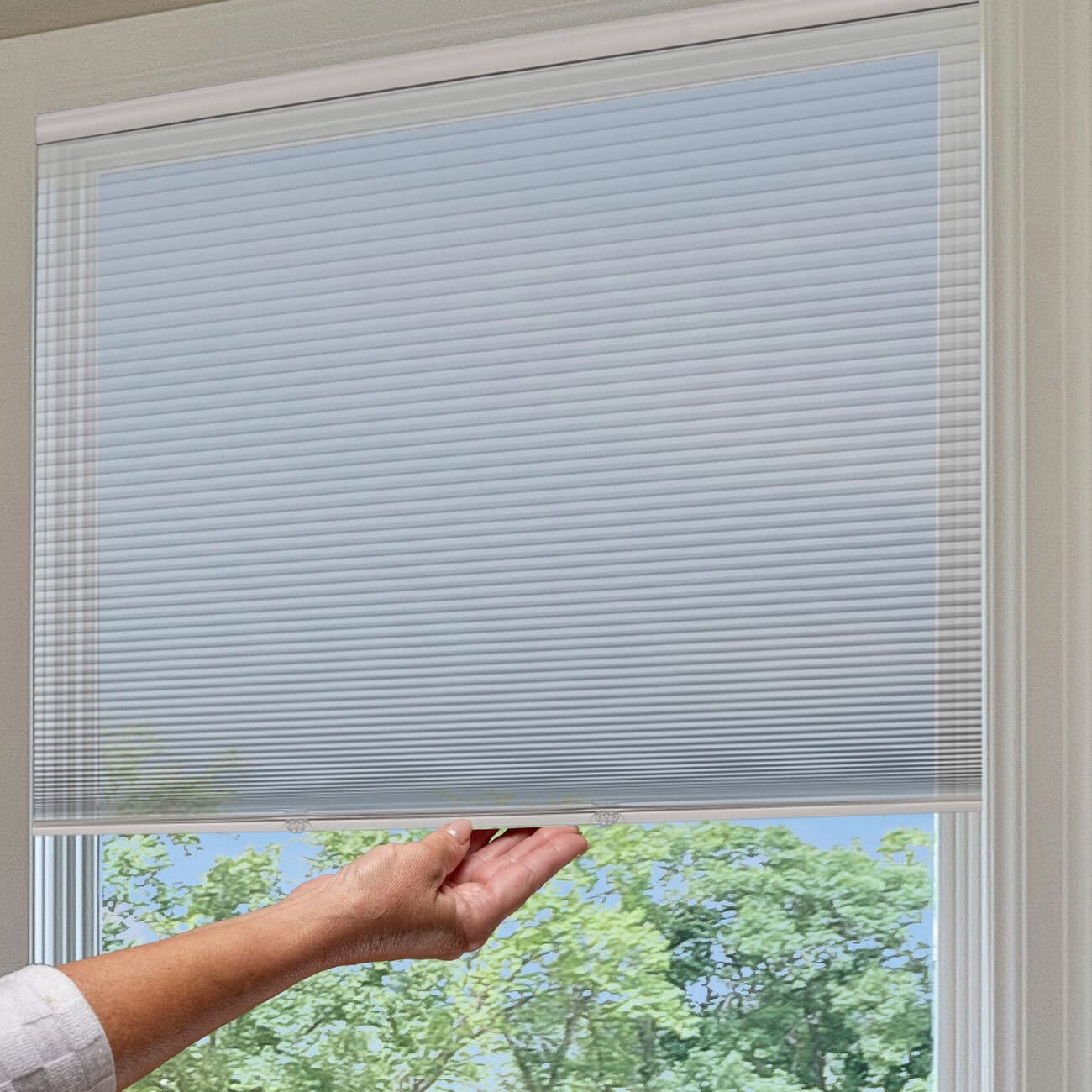 Close-up of a motorized cellular shade in a window, with a hand adjusting the shade, showcasing modern window treatment technology.