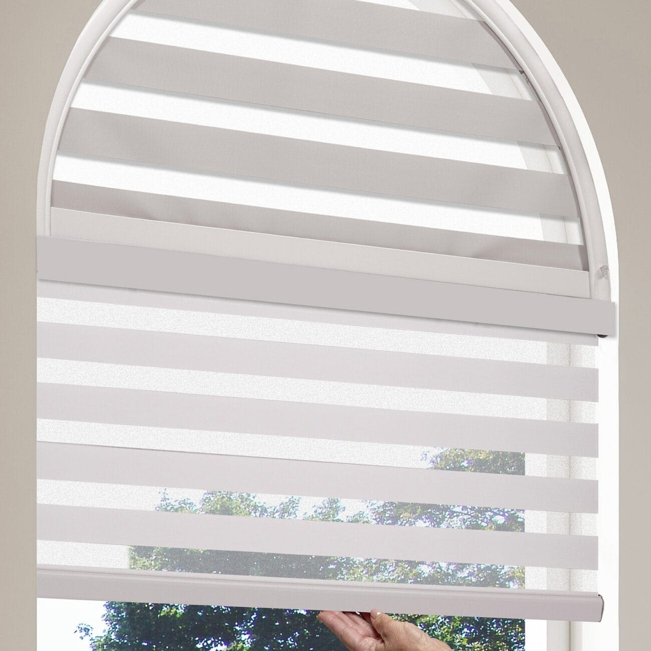 Close-up of a motorized dual shade window with remote control, showing horizontal white shades in an arched window frame.