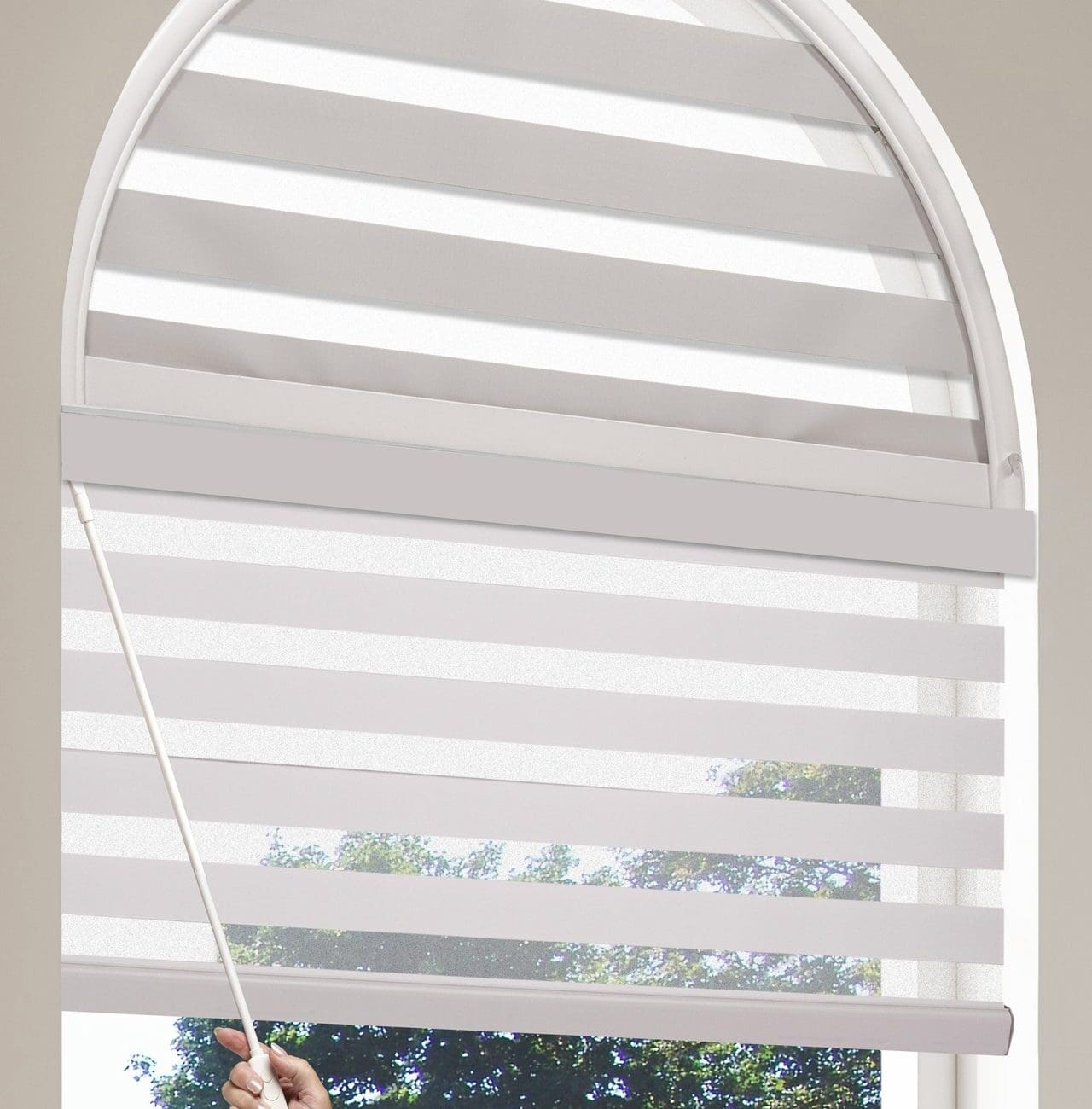 Close-up of Maxxmar motorized dual shades installed in an arched window, with a hand operating the remote control.