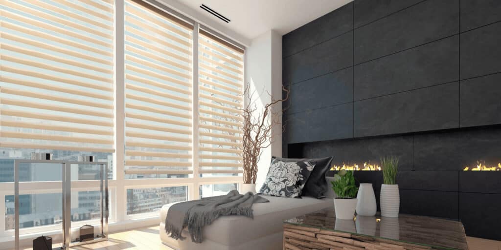Bright, spacious living room featuring expansive windows with blinds, contemporary black accent wall, cozy sofa with cushions, and decorative plants creating a welcoming atmosphere.
