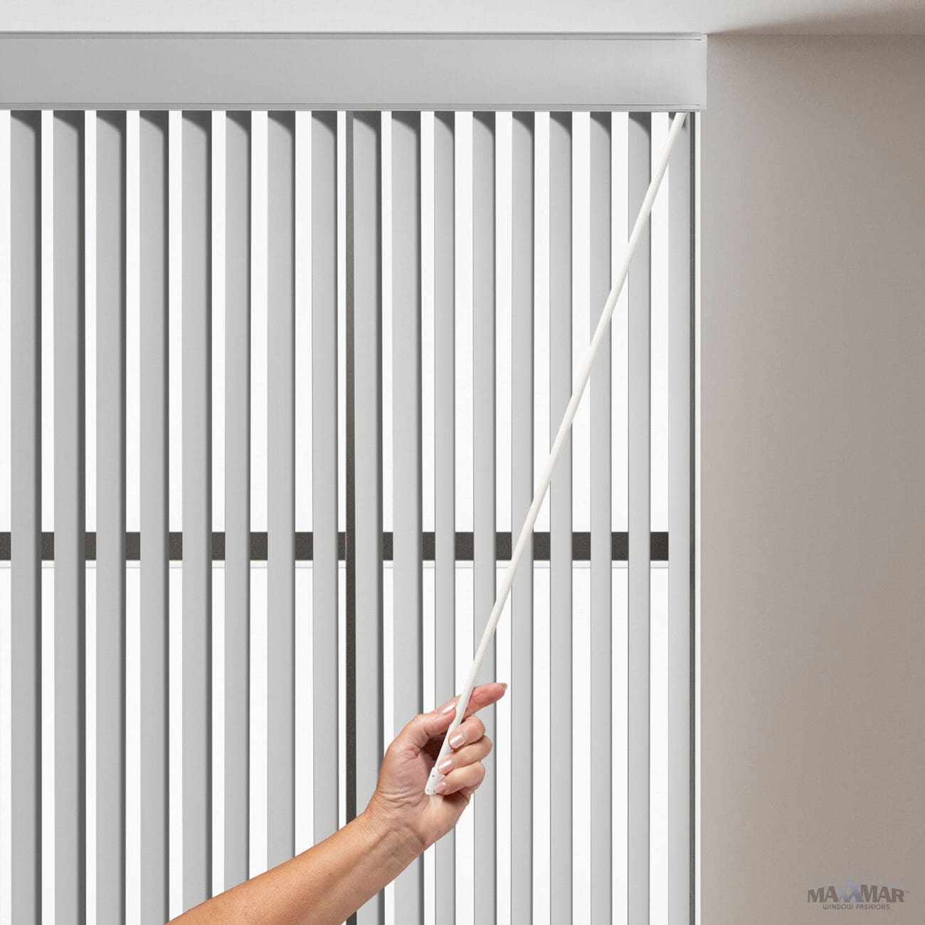 Close-up of a hand using a PVC wand control to operate vertical blinds in a modern interior.