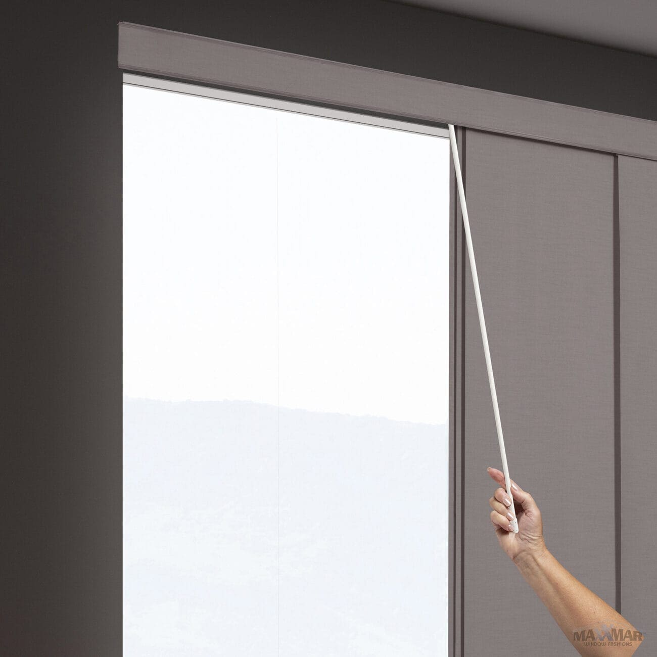Close-up of a hand using a wand control to operate a window blind or curtain in a modern interior setting.