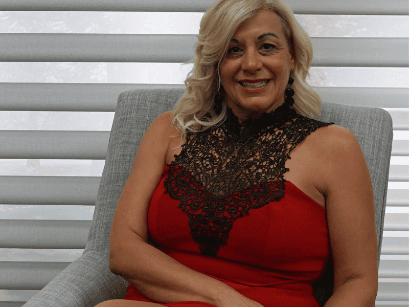 Untitled design (3) Elegant woman wearing a red dress with black lace detailing in a modern home setting.